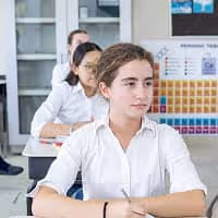 Estudiantes jóvenes sentados en un aula, prestando atención hacia adelante.